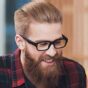 digital konnecter services A man with glasses and a full beard is smiling. He has neatly styled blonde hair and is wearing a red and black plaid shirt. The background is softly blurred, showing a mix of blue and wooden tones. providing digital services