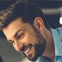 digital konnecter services A smiling man with a beard and short hair looks down. He is wearing a light blue shirt. The background is blurred. providing digital services